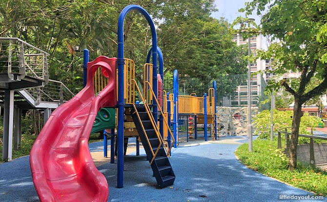 Red slides and a grey climbing wall in the central play area at Tampines Leisure Park.