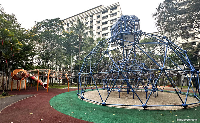 A large blue climbing pyramid with rope nets and an elevated playhouse at Circle Green Park.