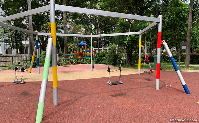 A hexagonal swing frame with coloured posts on red play surfacing at Circle Green Park.