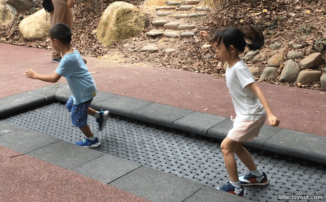 Two children on the elongated in-ground Forest Trampoline at Jacob Ballas Children’s Garden.