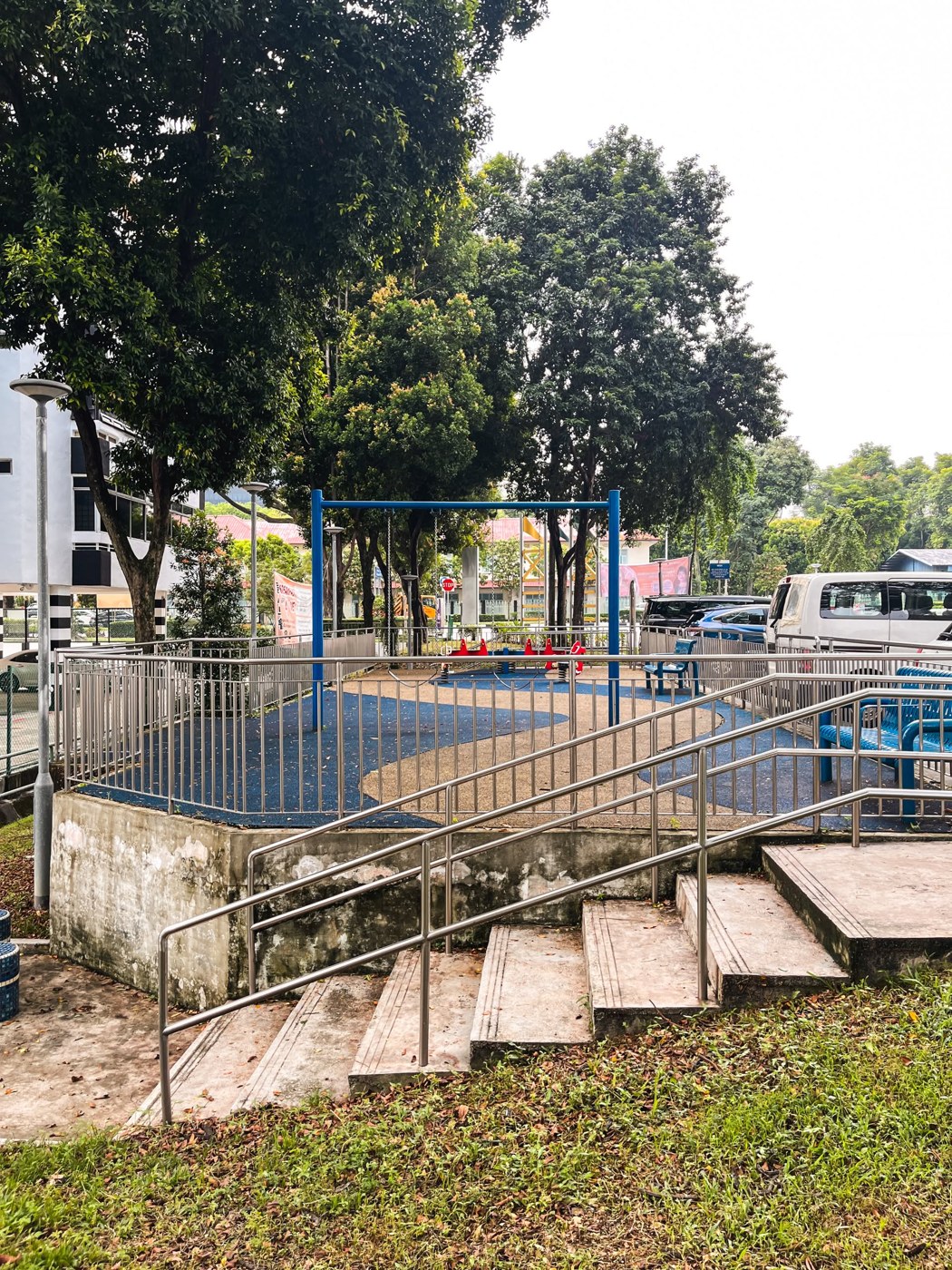 Blue swing frame and red seats at Moulmein View Playground, beside the car park and access ramp