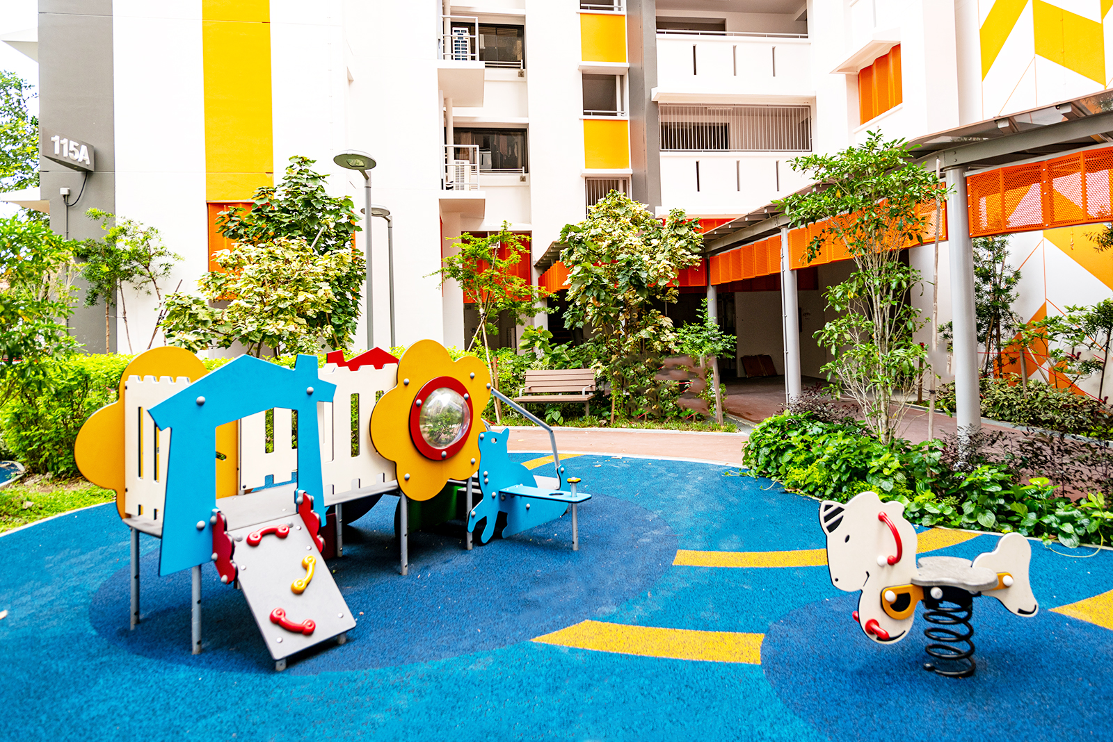 Low slide, play panels and spring rider on blue surfacing at the Kallang Residences toddler play area.