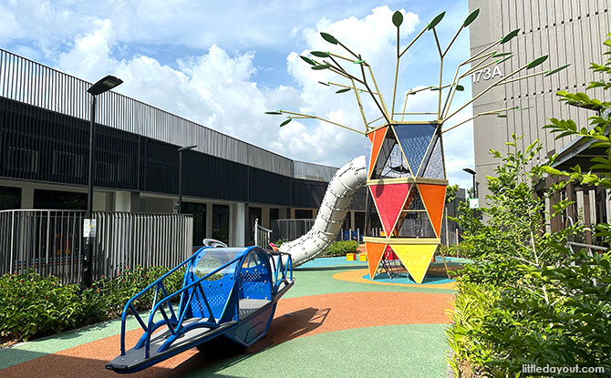 A colourful triangular-panel tower with a tube slide and blue seesaw at Rivervale Shores.