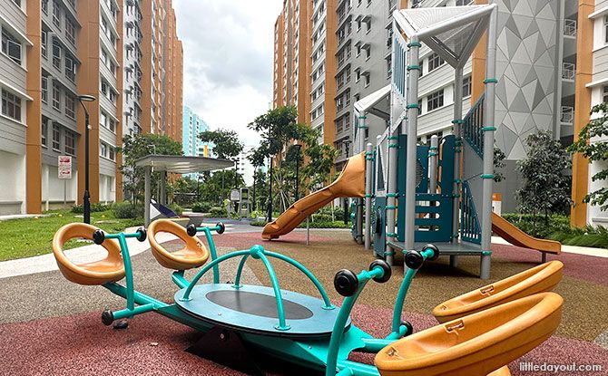 A four-seat seesaw beside a grey play tower and orange slides at Jurong West Jewel.