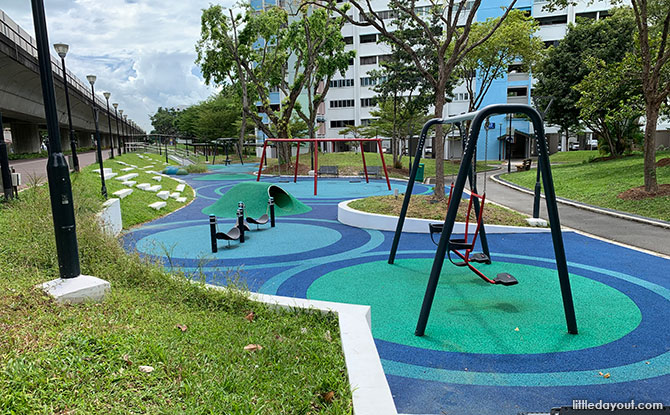 A five-sided swing frame on blue and green surfacing beside the MRT viaduct.