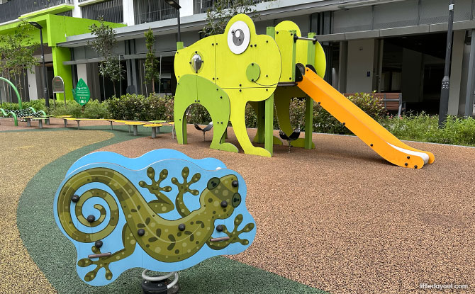 A green frog-themed play structure with an orange tongue slide and low balancing obstacles.
