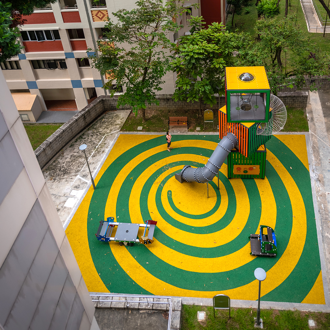 Small play tower with a curved tube slide on a square green-and-yellow spiral play surface at Block 229 Bishan Street 23.