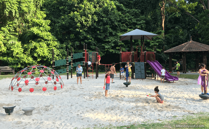 A sandy playground with a climbing tower and purple slides among trees at Bukit Batok Nature Park.